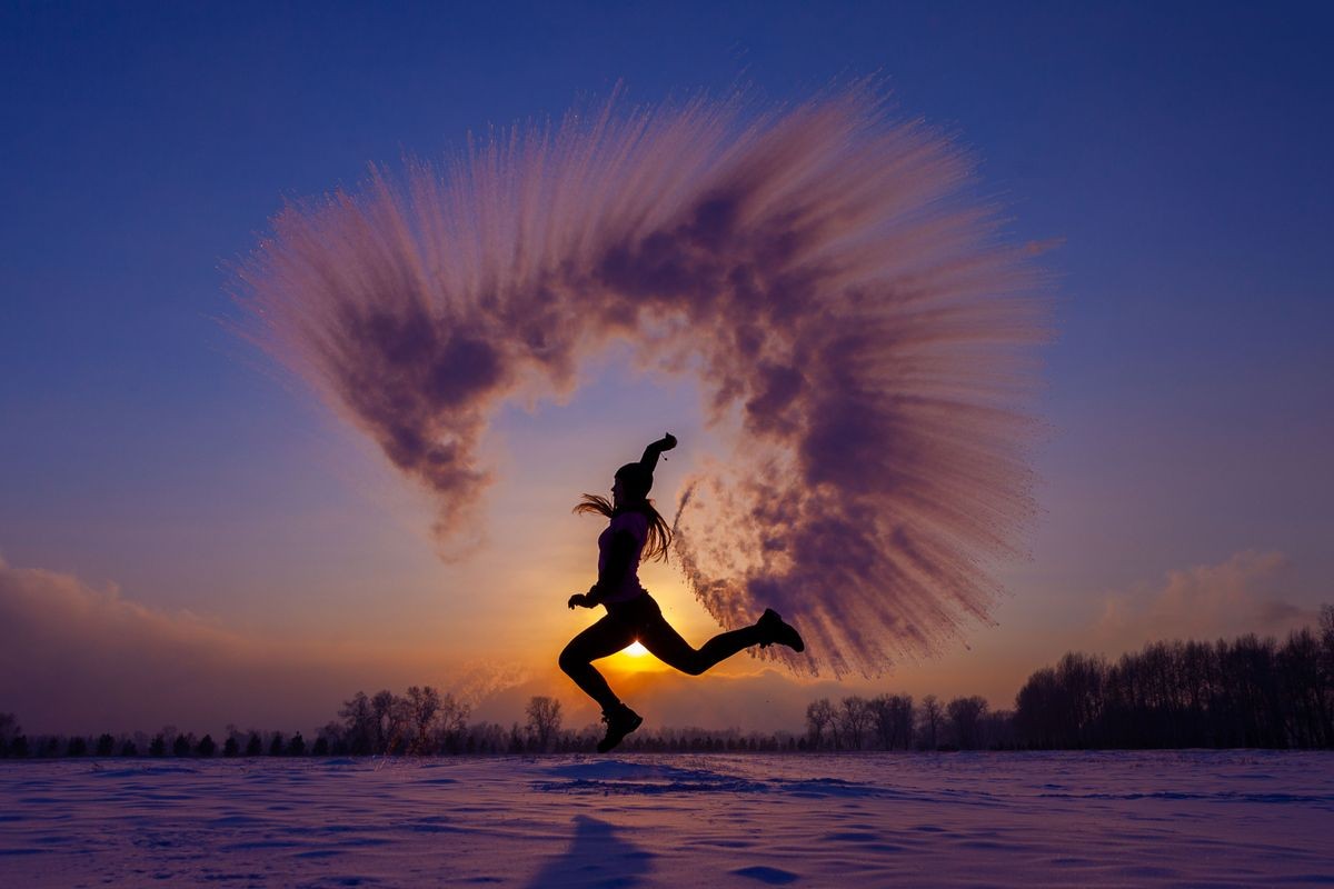 Silhouette of a sports girl at sunset in winter. Woman splashed boiling water on cold air.